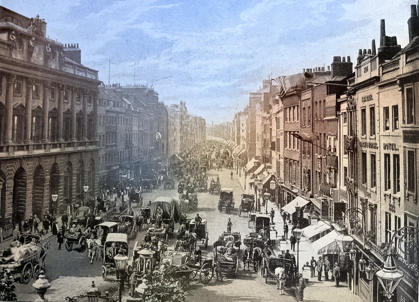 A colorized photo of a busy street in London, England in the late 1800s. The street is lined with buildings on both sides and is filled with horse-drawn carriages and people. The buildings are tall and ornate, with many windows. The street is cobblestone and there are street lamps along the sides. The sky is clear and the photo is taken from a high angle, looking down on the street.